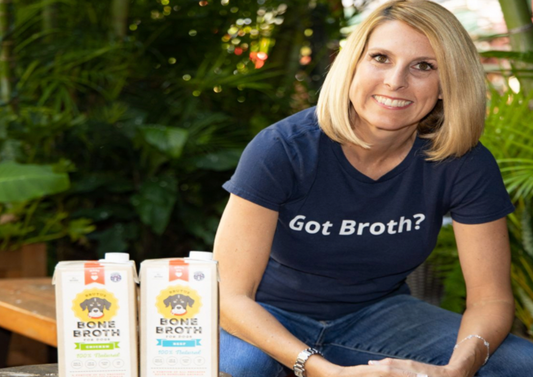 Co-founder Kim Hehir sitting with a box of Beef Brutus Bone Broth and Chicken Brutus Bone Broth
