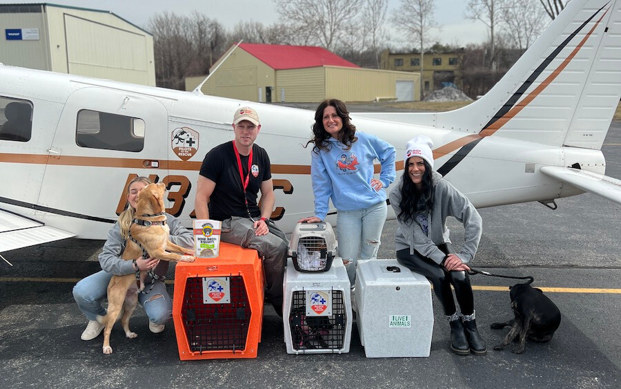 Pilots To The Rescue team standing in front of an airplane with crates and dogs