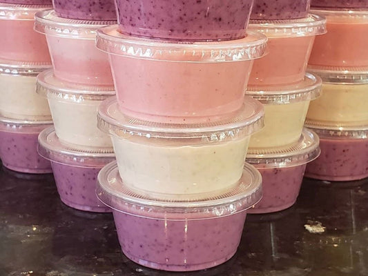 Front view of stacked 3 ounce cups of frozen dog treats showcasing pink, purple, and pale yellow layers with clear lids on a dark counter