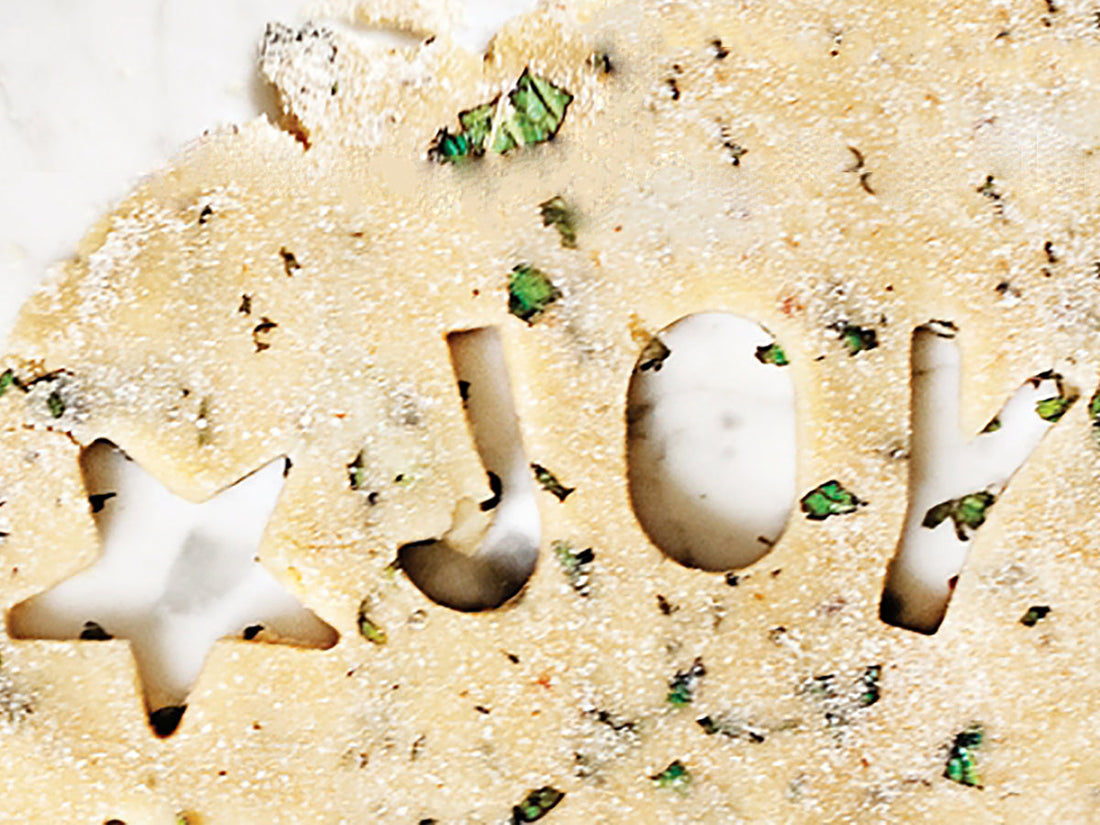 Close-up of Puppermint dog treat dough with JOY and star cutouts speckled with chopped mint on a white surface