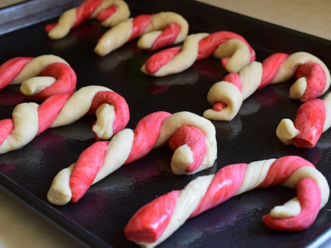 Close up of candy cane dog treats showcasing red and white twisted dough on a black baking sheet