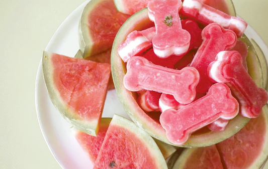 Top view of bone-shaped frozen watermelon treats showing pink-and-white layered centers served in a hollowed watermelon with watermelon slices on a white plate