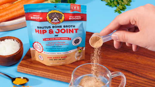 Brutus Bone Broth Hip & Joint pouch beside bowls; hand sprinkling powder from scoop into clear mug