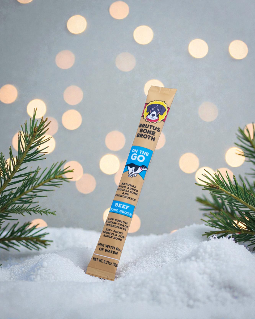 Beef Brutus Broth on the Go Stick with pine tree branches, snow, and twinkly lights in the background