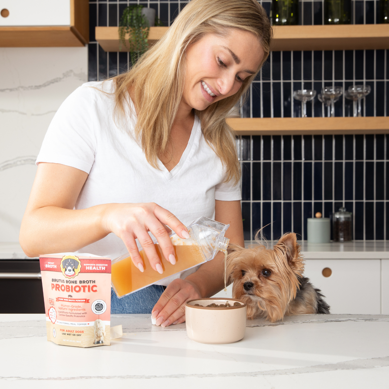 Woman pouring the Brutus Broth Probiotic Pork Broth for her dog in a kitchen setting.