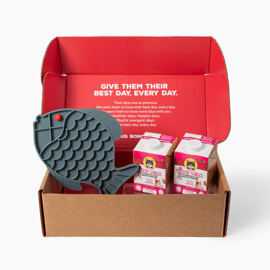 Front view of Goat Milk Club box showing fish-shaped silicone lick mat and two goat milk cartons with red interior headline